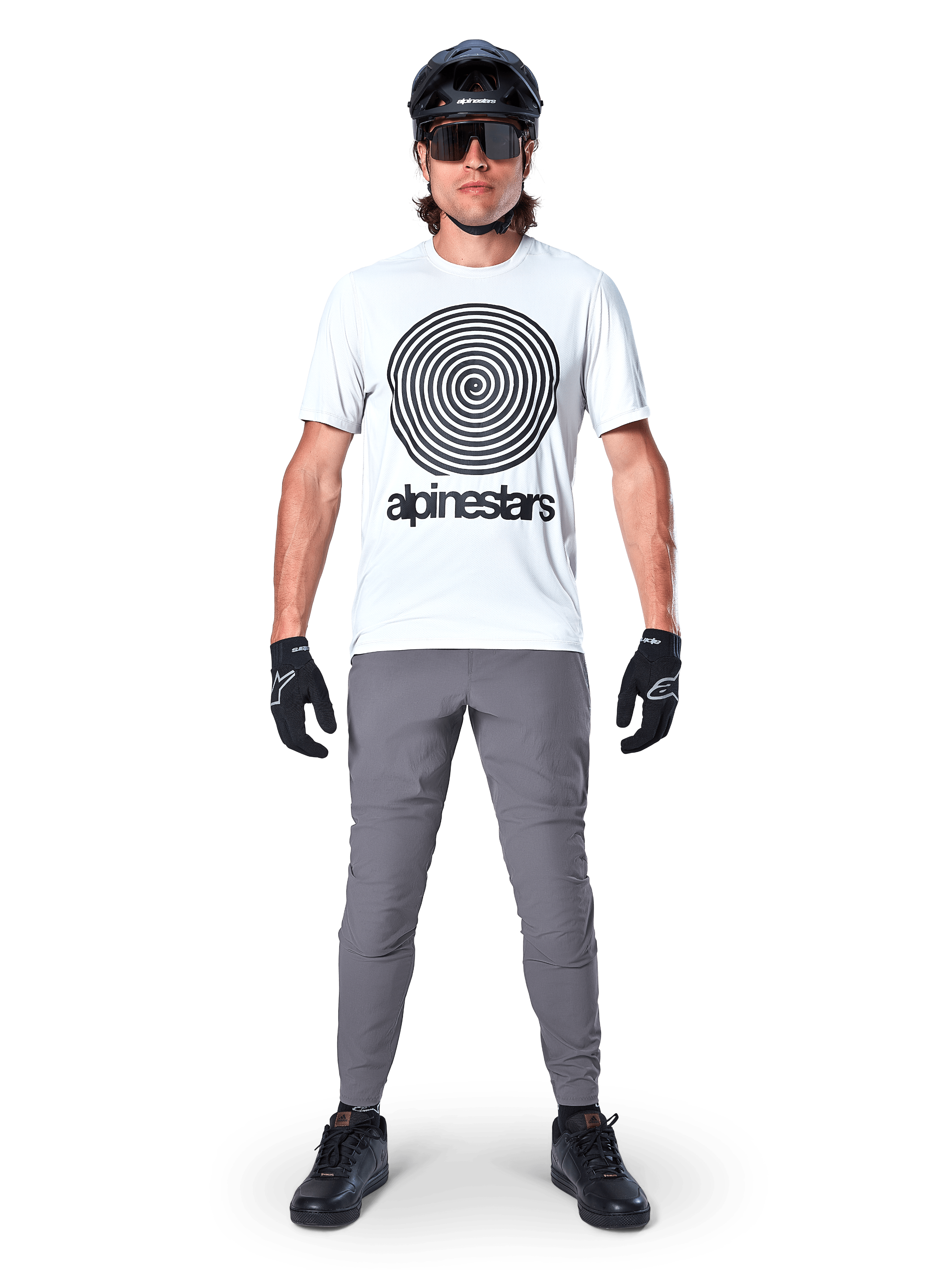 Vététiste portant le maillot Alpinestars A-Dura Oscar à manches courtes, White Dove avec un grand logo spirale noir, associé à un pantalon gris, un casque noir, des lunettes de soleil et des gants noirs, équipement de VTT haute performance