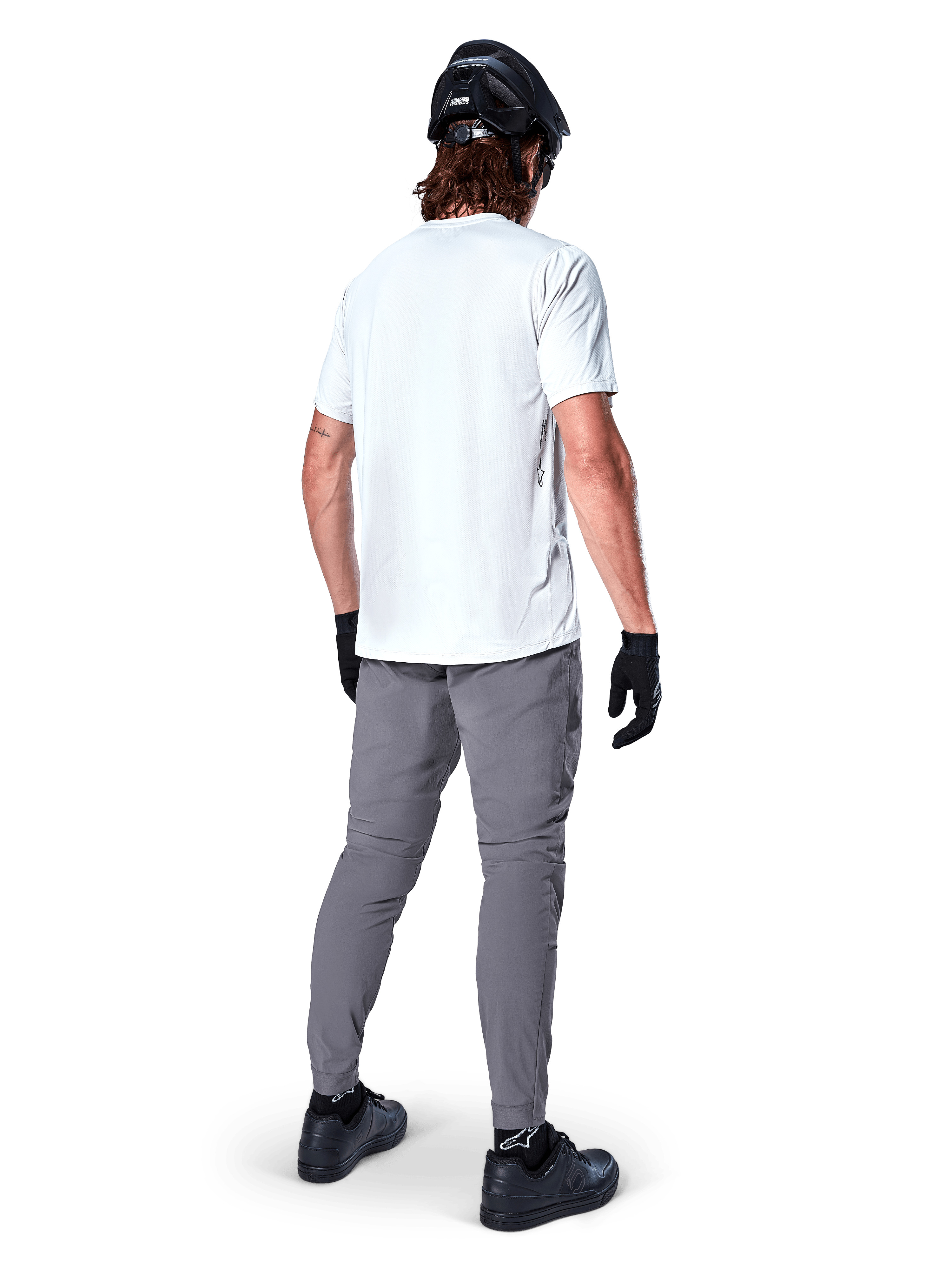 Maillot à manches courtes Alpinestars A-Dura Oscar en White Dove, vue de dos porté par un cycliste avec pantalon de cyclisme gris, casque noir et gants, équipement technique de VTT pour le trail tout-terrain