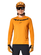 Alpinestars A-Dura Rocker Langarmtrikot in Dunkelgold, mit schwarzem Wortmarken-Logo auf der Brust, getragen mit einem passenden goldenen Helm und Handschuhen für Mountainbike-Performance.