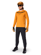 Alpinestars A-Dura Rocker Langarmtrikot, Radsport-Trikot in Dark Gold, getragen mit passendem MTB-Helm und schwarzer Hose, mit schwarzem Wortmarken-Logo auf der Brust, abgestimmte Performance-Ausrüstung für Offroad-Mountainbiking