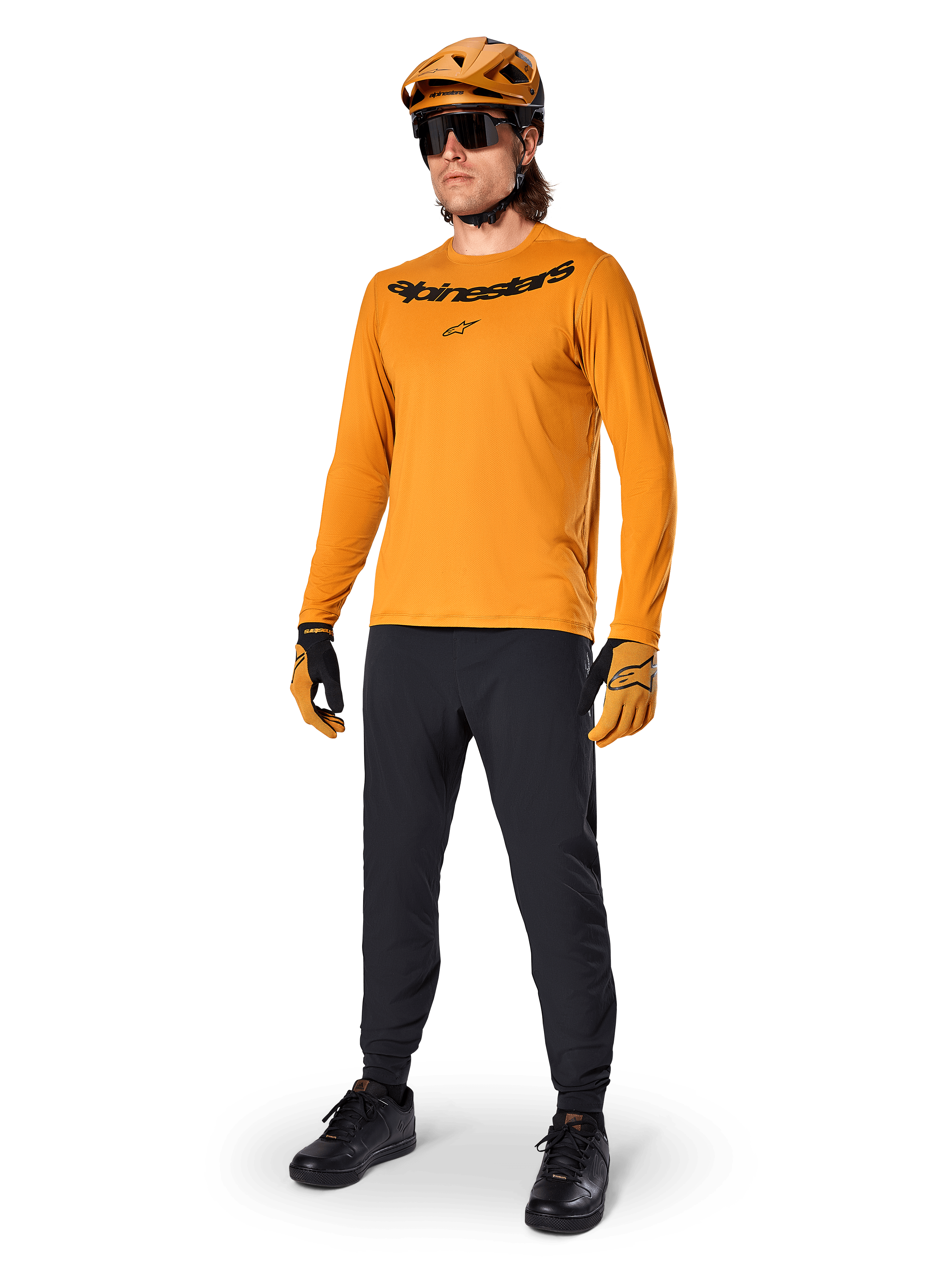 Alpinestars A-Dura Rocker Langarmtrikot, Radsport-Trikot in Dark Gold, getragen mit passendem MTB-Helm und schwarzer Hose, mit schwarzem Wortmarken-Logo auf der Brust, abgestimmte Performance-Ausrüstung für Offroad-Mountainbiking