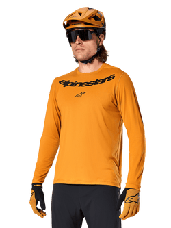 Alpinestars A-Dura Rocker Langarmtrikot, MTB-Mountainbike-Trikot, Dunkelgold, Person trägt Trikot mit passendem Helm und Handschuhen, sportlich abgestimmter Look mit Alpinestars-Wortmarke auf der Brust