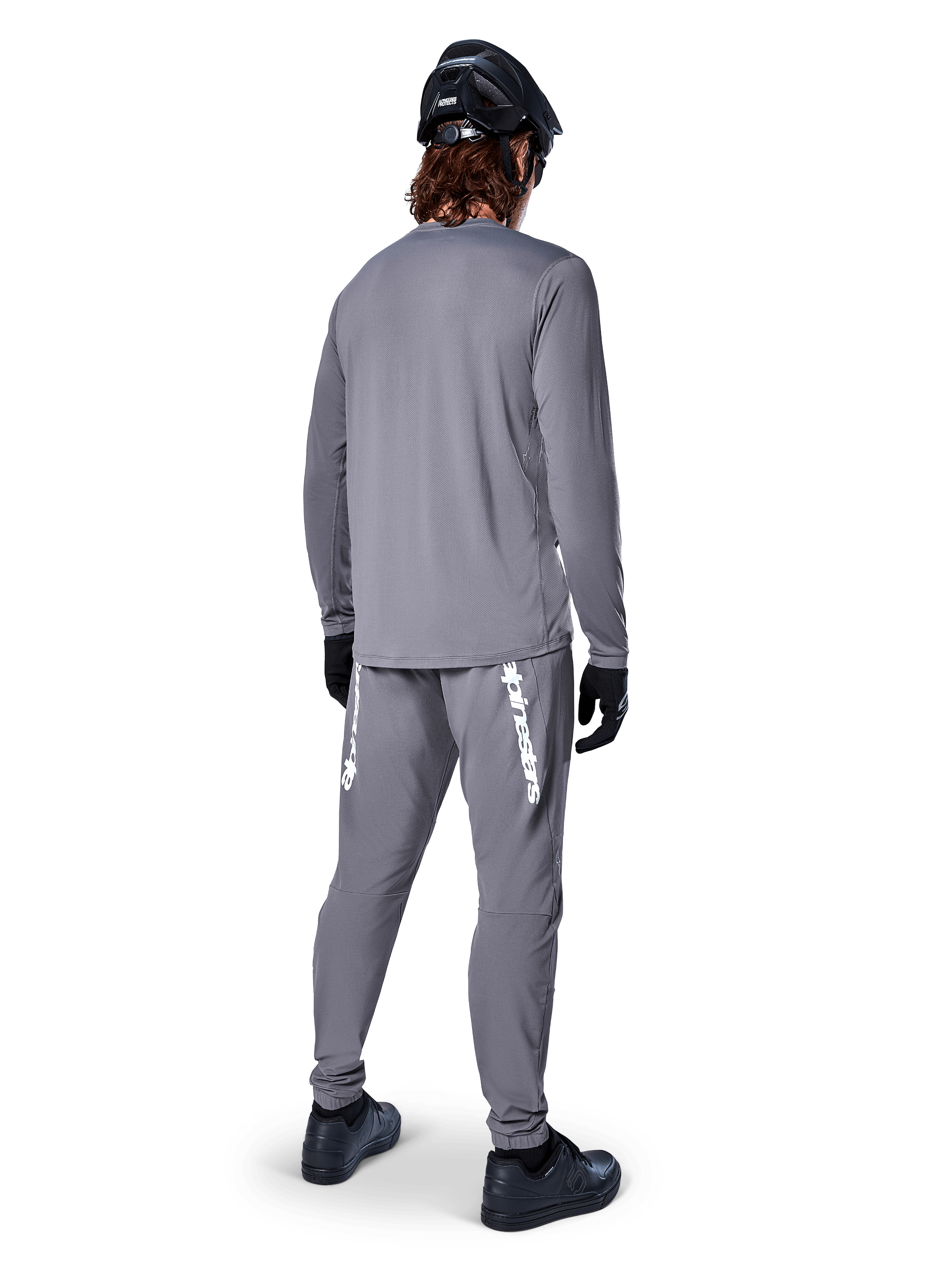 Alpinestars A-Dura Rocker Jersey met lange mouwen, donkergrijs, achteraanzicht van model met bijpassende grijze MTB-broek, zwarte helm en zwarte handschoenen, professioneel ontwerp voor mountainbikekleding
