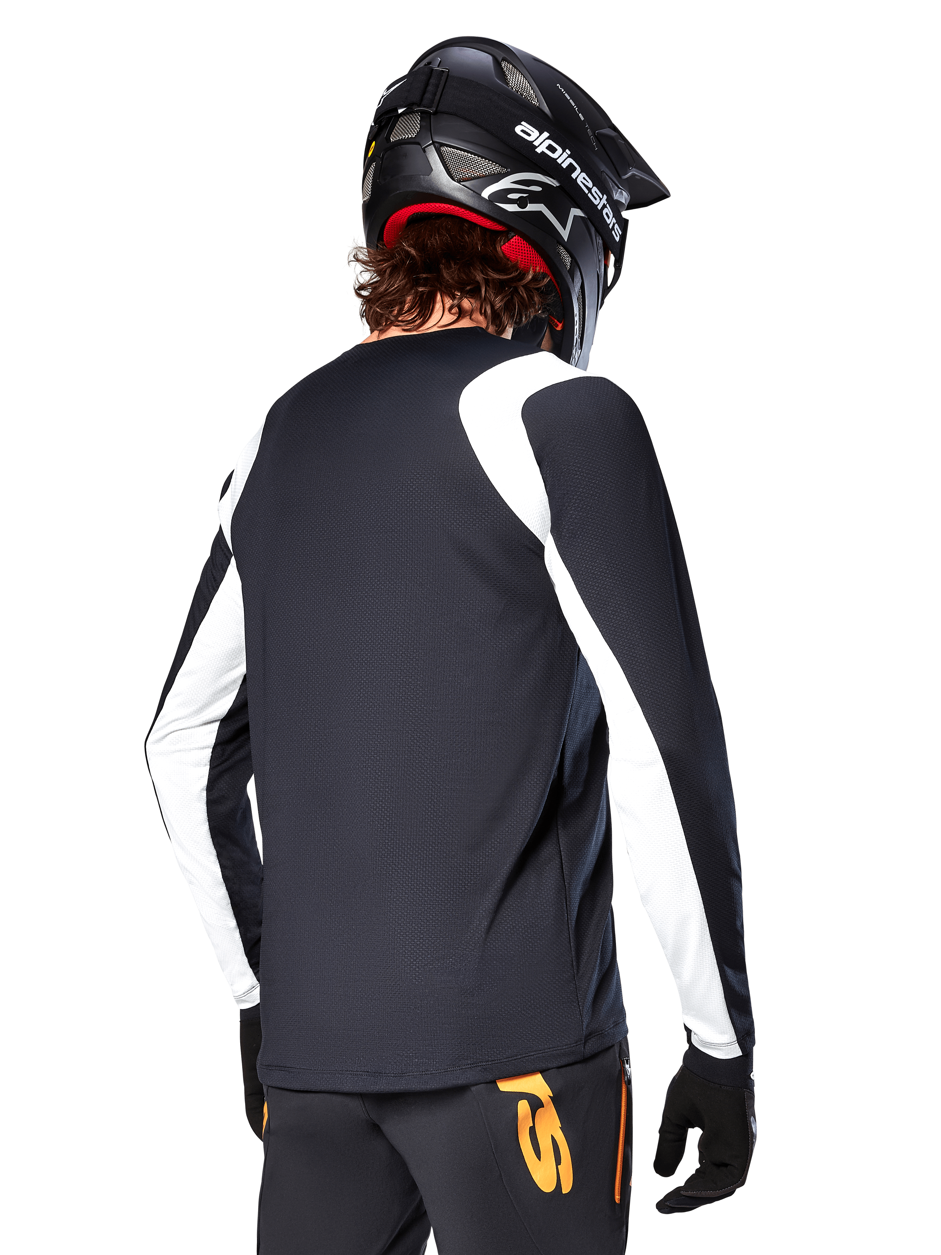 Cycliste de VTT portant un maillot à manches longues Alpinestars A-Supra Oscar, noir avec des empiècements blancs sur les épaules et les manches, vue de dos, casque et gants noirs, pantalon avec des touches d'orange, équipement de cyclisme tout-terrain durable