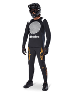 Cycliste de VTT portant le maillot à manches longues Alpinestars A-Supra Oscar noir, graphique en spirale Oscar vintage blanc, pantalon noir avec logos d'étoiles orange, casque intégral noir avec masque et gants noirs, équipement de VTT professionnel