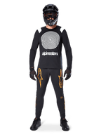 Mannequin homme portant un équipement complet de VTT, maillot à manches longues Alpinestars A-Supra Oscar noir avec graphique en spirale blanc sur la poitrine, pantalon noir avec logos étoiles orange, casque intégral noir et masque, gants et chaussures noirs, tenue coordonnée pour la pratique du VTT en gravité