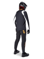 Maillot à manches longues Alpinestars A-Supra Oscar, noir avec empiècements blancs sur les manches, porté de dos par un cycliste VTT avec un casque intégral noir et un pantalon noir arborant des logos orange, vêtement de cyclisme pour le VTT de descente (gravity)