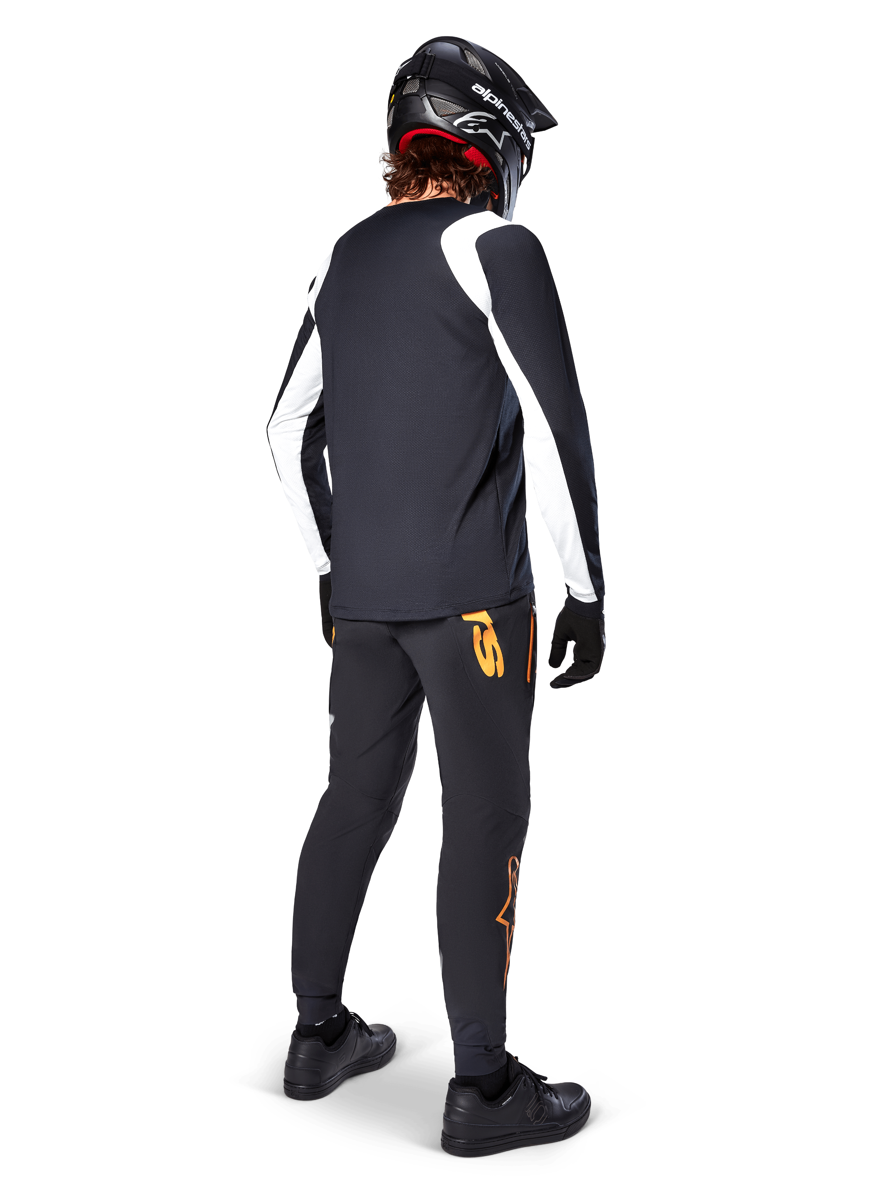Maillot à manches longues Alpinestars A-Supra Oscar, noir avec empiècements blancs sur les manches, porté de dos par un cycliste VTT avec un casque intégral noir et un pantalon noir arborant des logos orange, vêtement de cyclisme pour le VTT de descente (gravity)