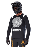 Alpinestars A-Supra Oscar Jersey à manches longues, maillot de VTT, noir et blanc, avec un motif en spirale blanc et le logo Alpinestars sur la poitrine, porté avec un casque intégral et un masque noirs, équipement de VTT haute performance