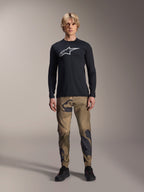Maillot à manches longues Alpinestars A-Dura Astar, noir, arborant un grand logo Astars blanc sur la poitrine, porté avec un pantalon camouflage et des chaussures noires, tenue de performance décontractée pour le VTT