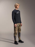 Alpinestars A-Dura Camo Pant, pantalon de VTT, camouflage brun, porté avec un maillot à manches longues A-Dura Astar noir et des chaussures noires, vêtement technique de VTT pour le trail.