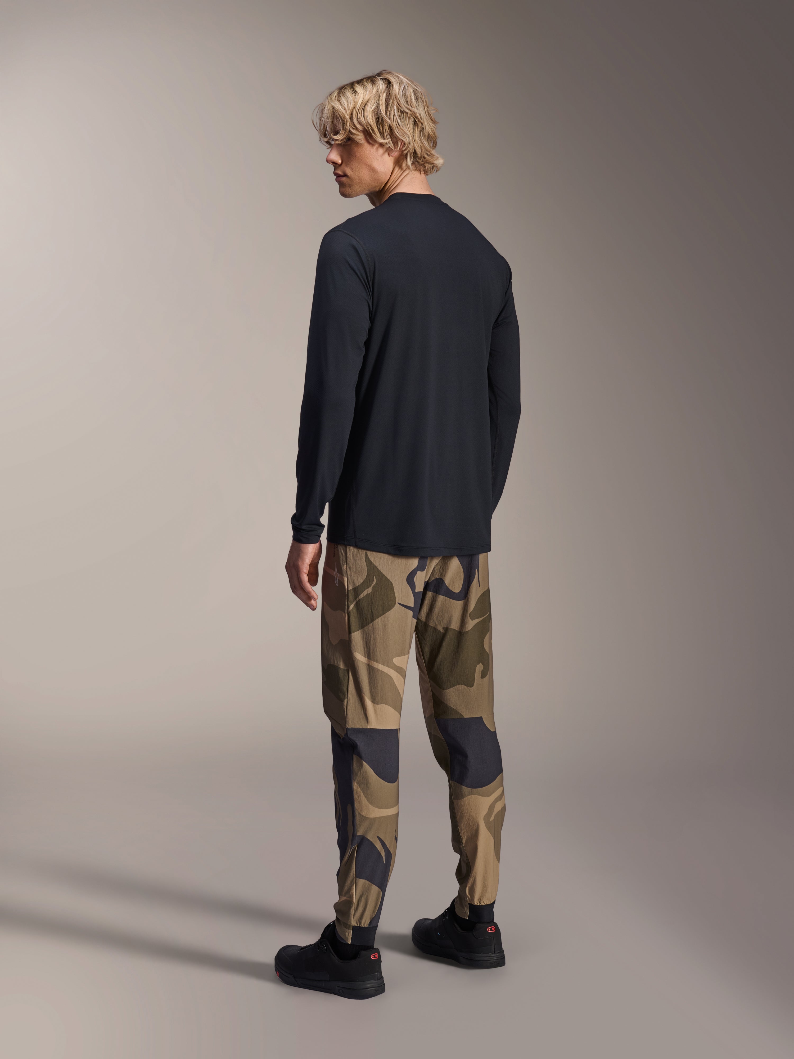Maillot à manches longues Alpinestars A-Dura Astar, noir, vue de dos sur un mannequin, porté avec un pantalon camouflage, équipement de performance VTT décontracté avec un pan arrière plus long et une coupe régulière