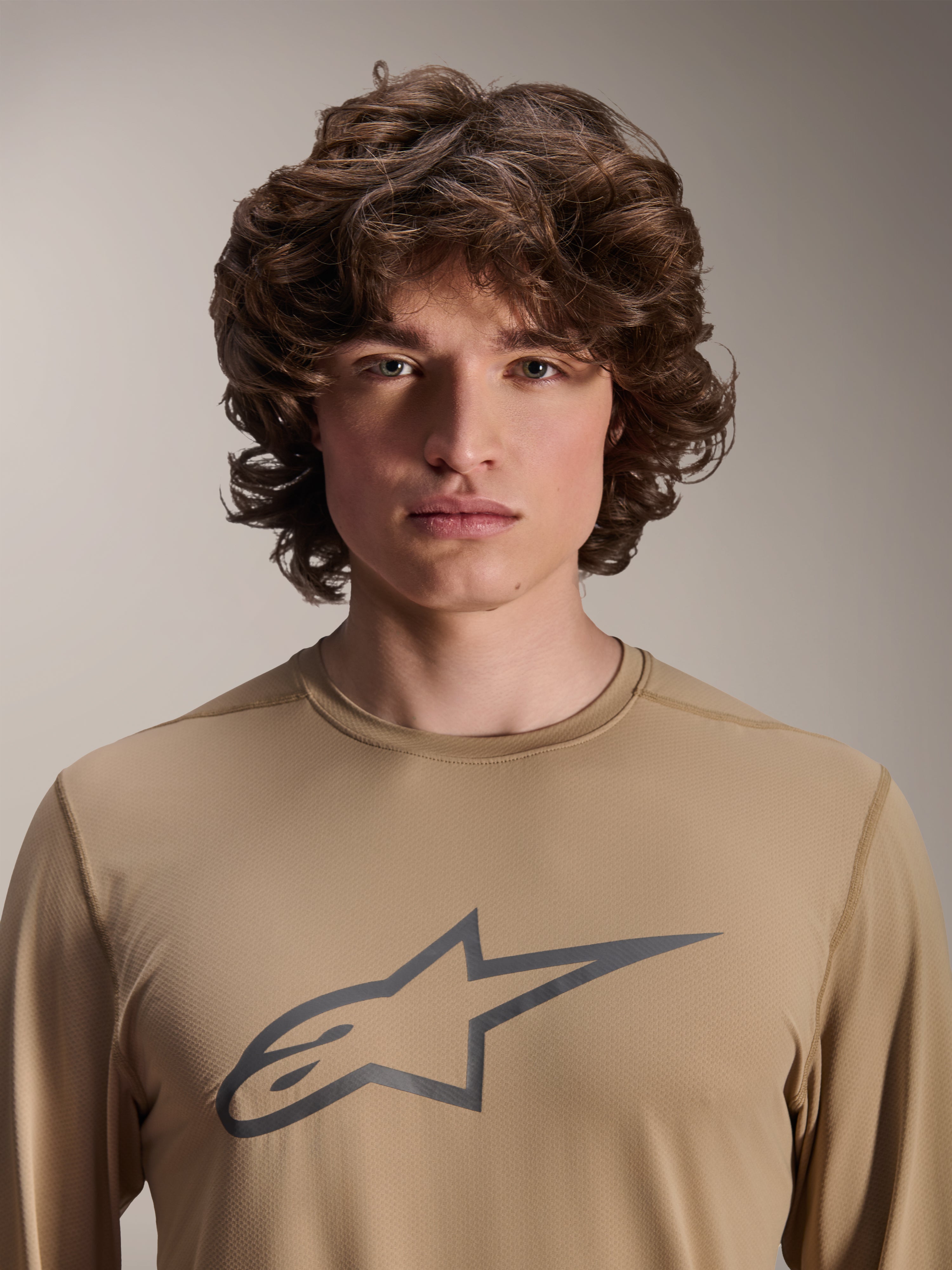 Alpinestars A-Dura Astar Jersey met lange mouwen, lichtbruin, gedragen door mannelijk model, met een groot Astars-logo op de borst, jacquard stoftextuur, casual mountainbikekleding