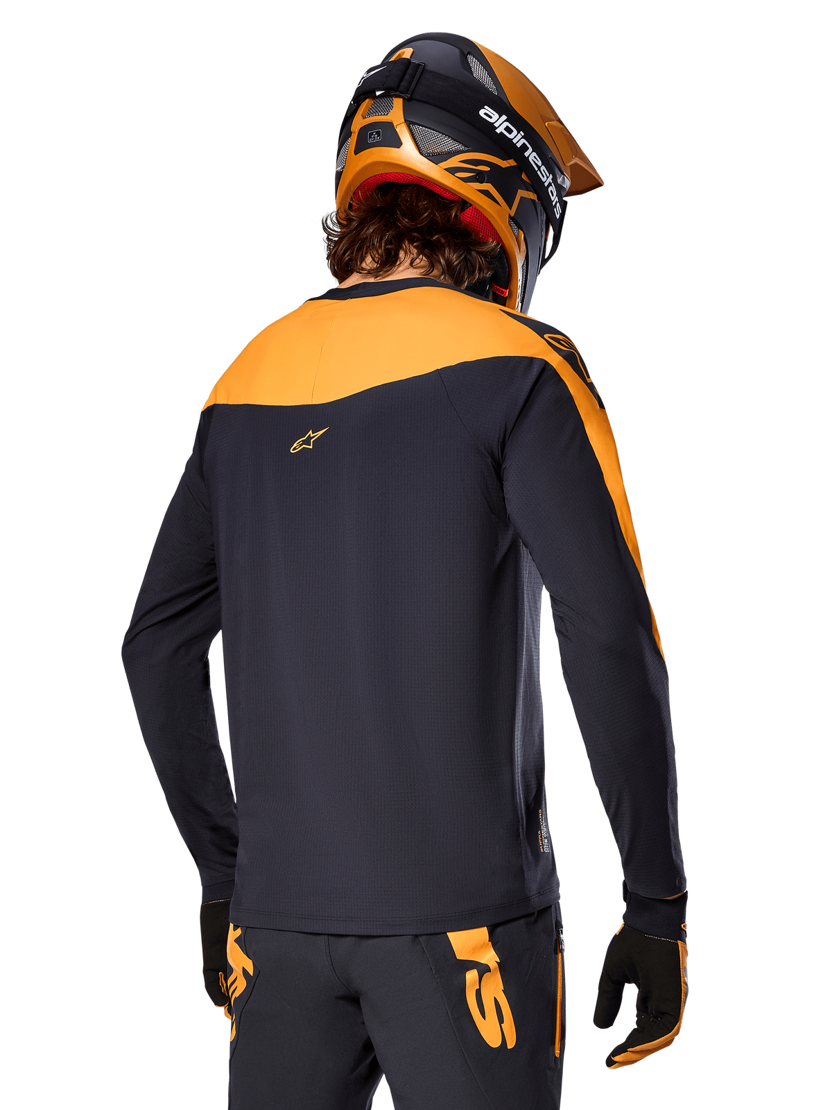 Maillot Alpinestars A-Supra Race - Manches longues, noir et orange, vue arrière d'un pilote portant un casque et un pantalon de VTT assortis, coupe performance avec texture micro-perforée, équipement de course VTT professionnel