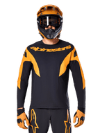 Pilote de VTT portant le maillot Alpinestars A-Supra Race à manches longues, noir avec graphismes orange et logo sur la poitrine, avec casque intégral orange assorti, masque noir et gants orange, tenue de course coordonnée pour la performance en VTT