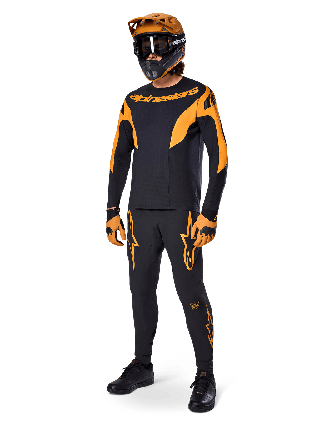Pilote de VTT en tenue de course complète, maillot A-Supra Race noir avec détails orange, pantalon noir assorti avec logos Alpinestars orange, casque intégral orange et noir avec masque, gants orange et noir, ensemble coordonné pour le VTT de compétition