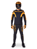 Pilote de VTT portant le maillot Alpinestars A-Supra Race à manches longues noir et orange, pantalon et gants assortis, casque intégral avec lunettes, tenue de VTT coordonnée pour la compétition et la performance tout-terrain