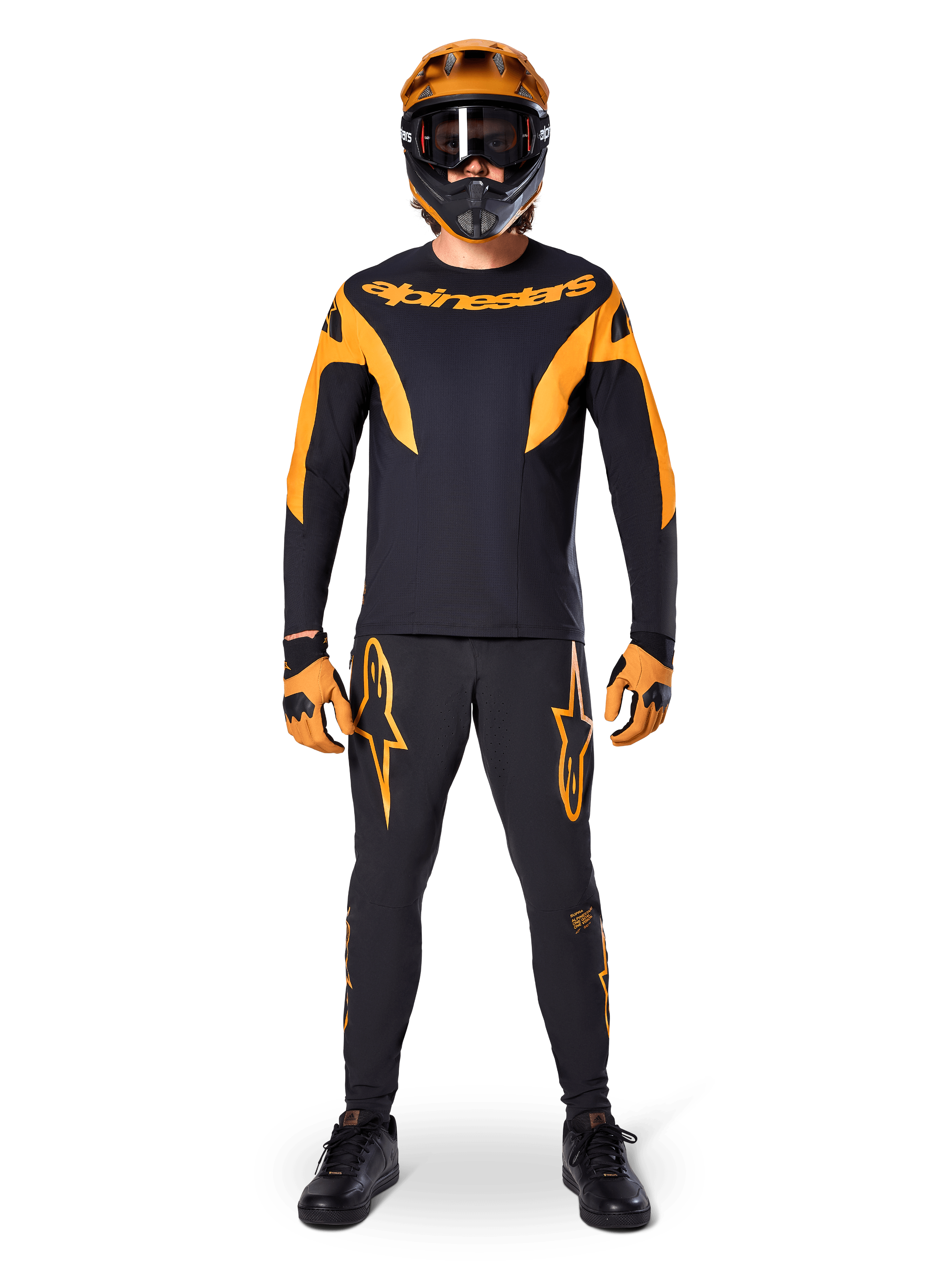 Pilote de VTT portant le maillot Alpinestars A-Supra Race à manches longues noir et orange, pantalon et gants assortis, casque intégral avec lunettes, tenue de VTT coordonnée pour la compétition et la performance tout-terrain