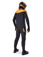 Maillot A-Supra Race - Manches longues, noir et orange, vue arrière d'un pilote portant un pantalon de VTT assorti, un casque orange et noir et des gants, équipement de performance pour la course de VTT