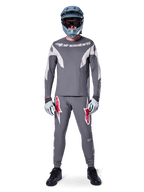 Pilote portant le maillot Alpinestars A-Supra Race - Manches longues en gris foncé, coordonné avec un pantalon gris assorti arborant des logos d'étoiles rouges, un casque gris avec lunettes et des gants gris clair, kit de VTT complet pour le cyclisme tout-terrain de performance