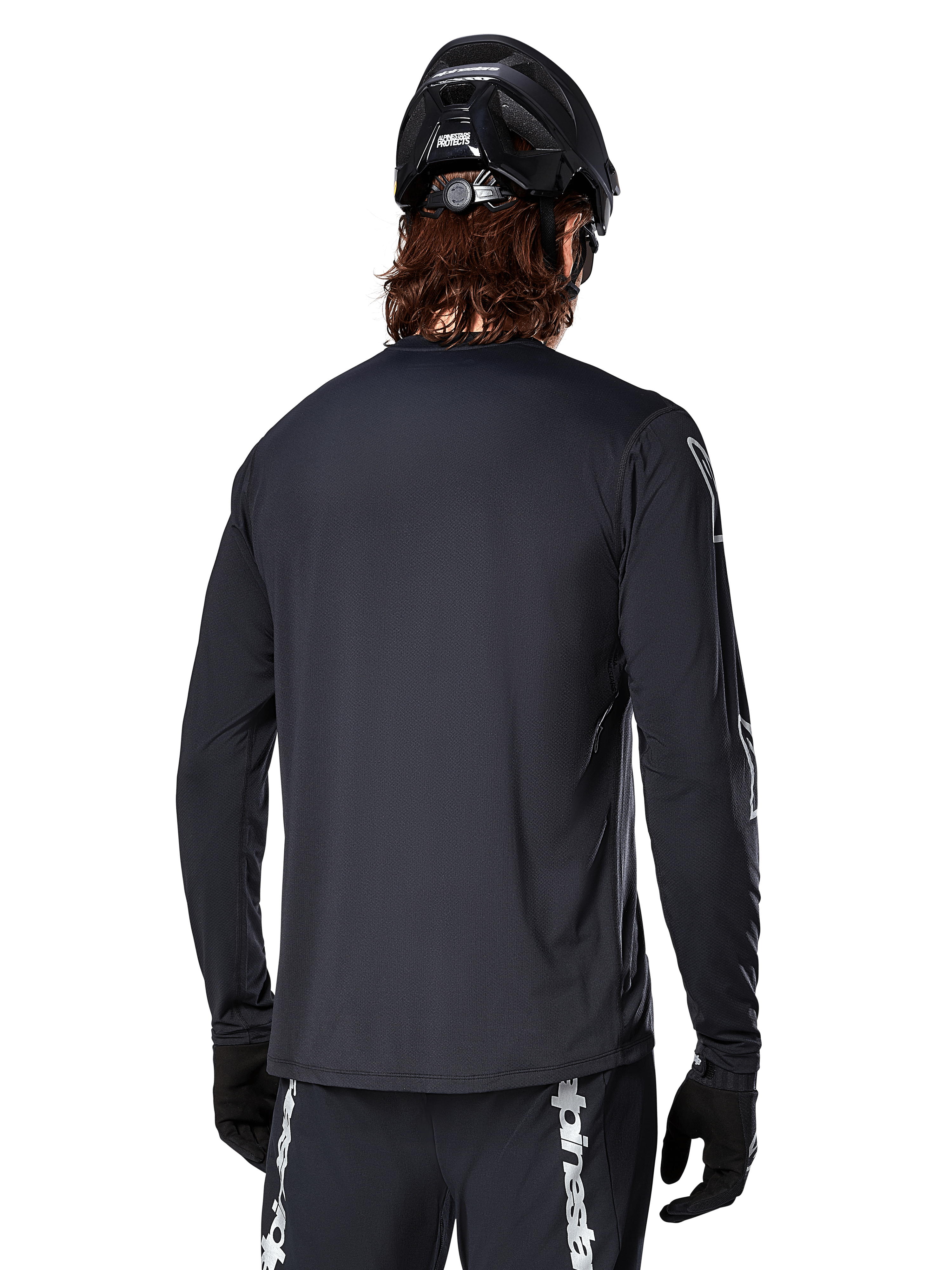 Maillot à manches longues Alpinestars A-Dura Switch, noir, vue arrière sur un cycliste portant un casque de VTT noir et des gants, doté d'un tissu jacquard technique et d'une coupe allongée dans le dos pour la pratique du tout-terrain