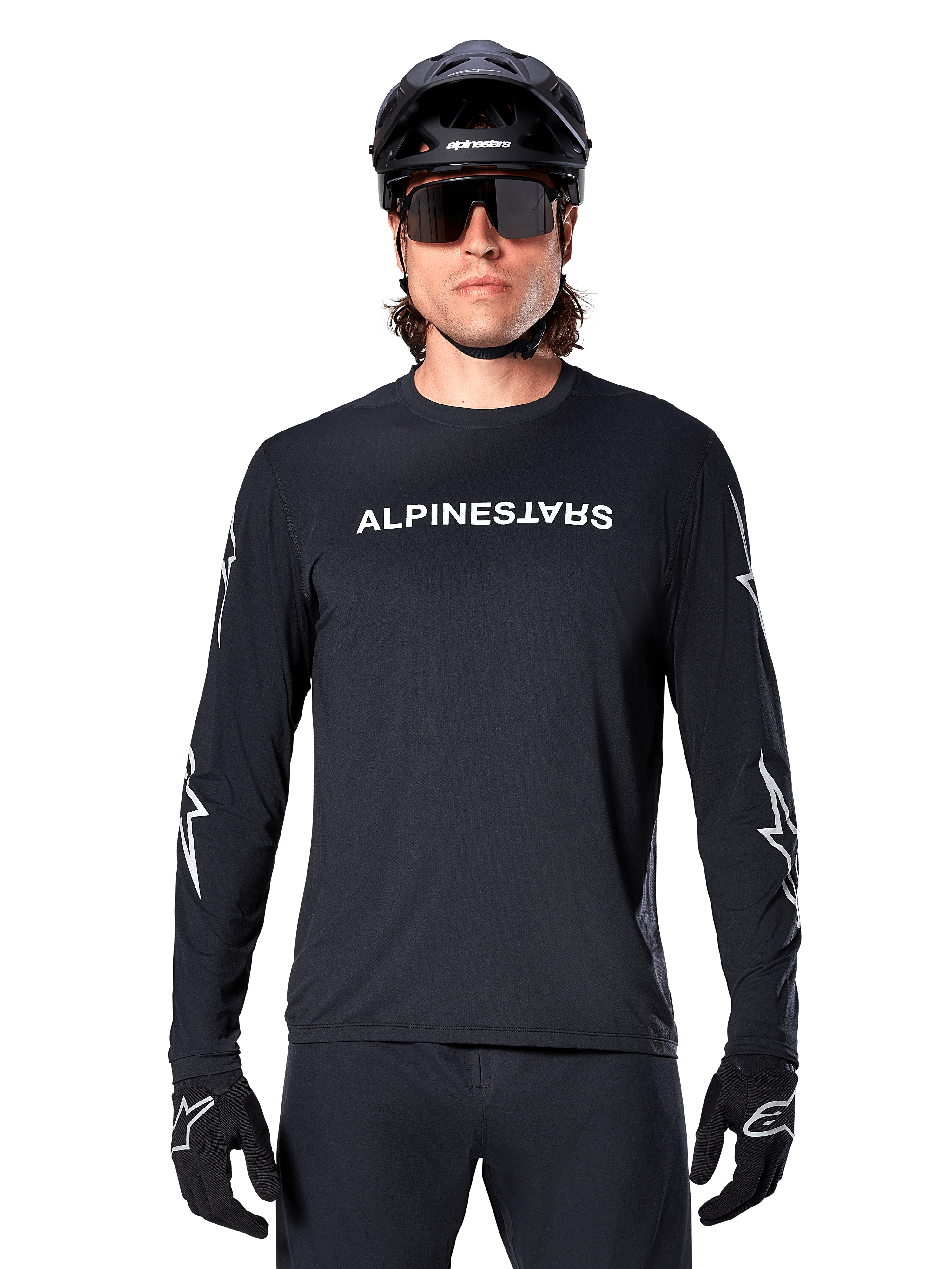 Maillot à manches longues Alpinestars A-Dura Switch, maillot de VTT noir, logo Alpinestars blanc sur la poitrine et graphismes d'étoiles sur les manches, porté avec un casque de VTT noir et des lunettes de soleil de performance, vêtement technique de trail