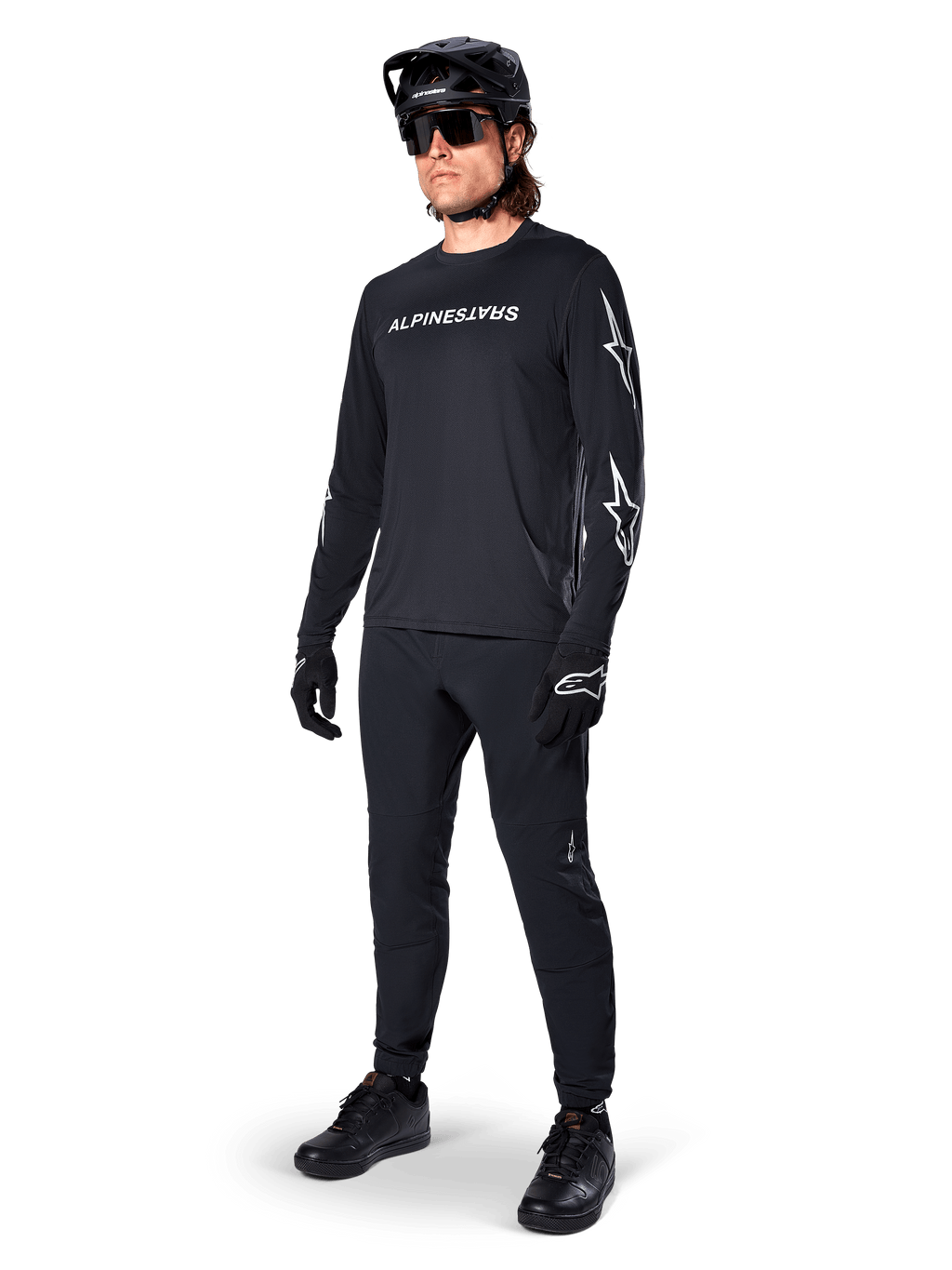 Maillot à manches longues Alpinestars A-Dura Switch, noir, maillot de VTT porté avec un pantalon, un casque et des gants noirs, avec logo lettrage blanc sur la poitrine et logos étoiles sur les manches, équipement de VTT coordonné pour le tout-terrain