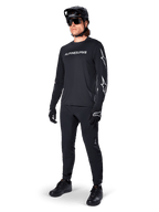 Maillot à manches longues Alpinestars A-Dura Switch, noir, maillot de VTT porté avec un pantalon, un casque et des gants noirs, avec logo lettrage blanc sur la poitrine et logos étoiles sur les manches, équipement de VTT coordonné pour le tout-terrain