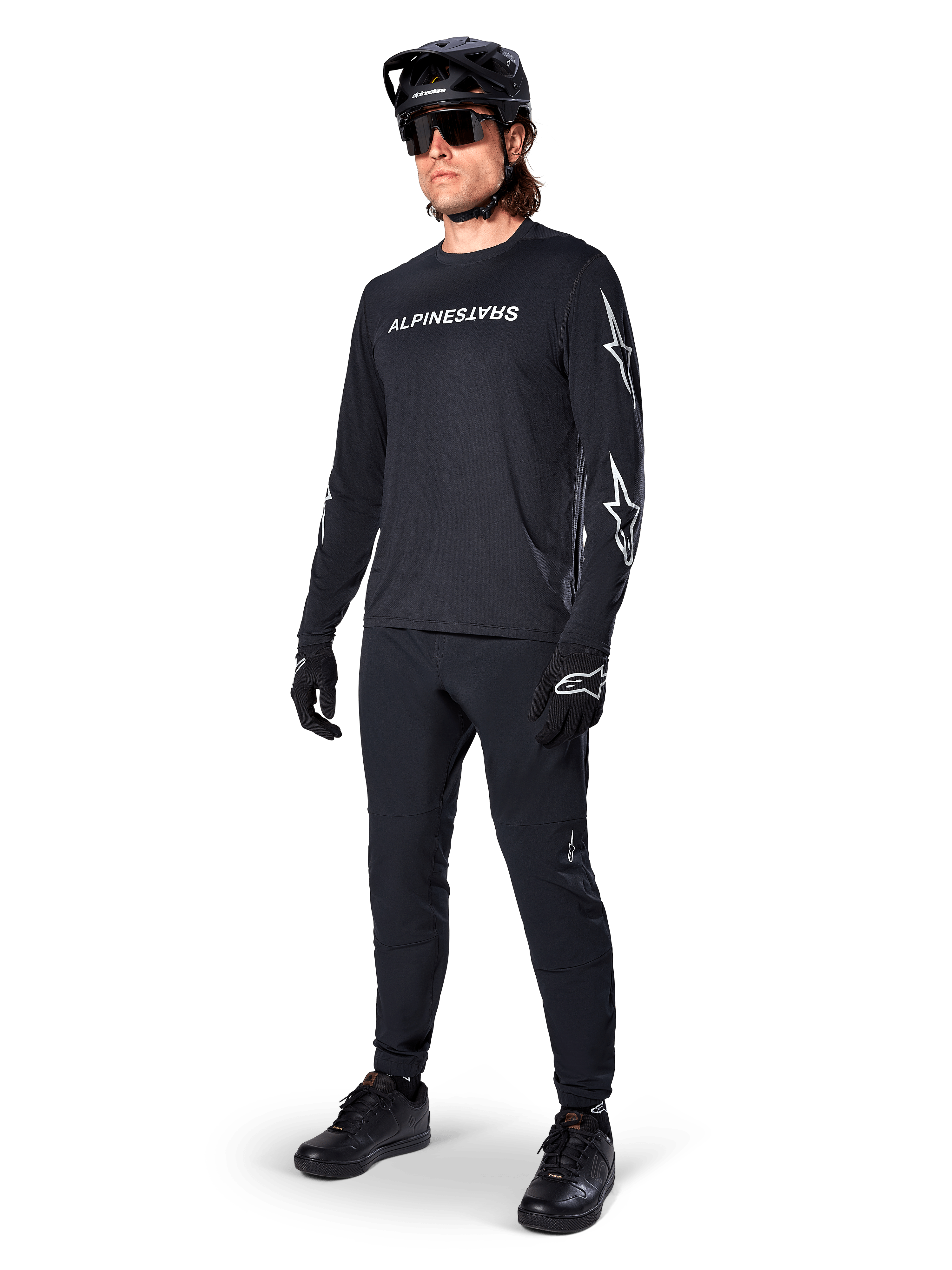 Maillot à manches longues Alpinestars A-Dura Switch, noir, maillot de VTT porté avec un pantalon, un casque et des gants noirs, avec logo lettrage blanc sur la poitrine et logos étoiles sur les manches, équipement de VTT coordonné pour le tout-terrain