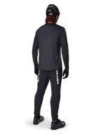 Maillot à manches longues Alpinestars A-Dura Switch, noir, vue arrière sur un cycliste, porté avec un pantalon noir arborant le marquage Alpinestars blanc, un casque noir et des gants, doté d'un pan arrière allongé pour une meilleure protection, vêtement de VTT haute performance