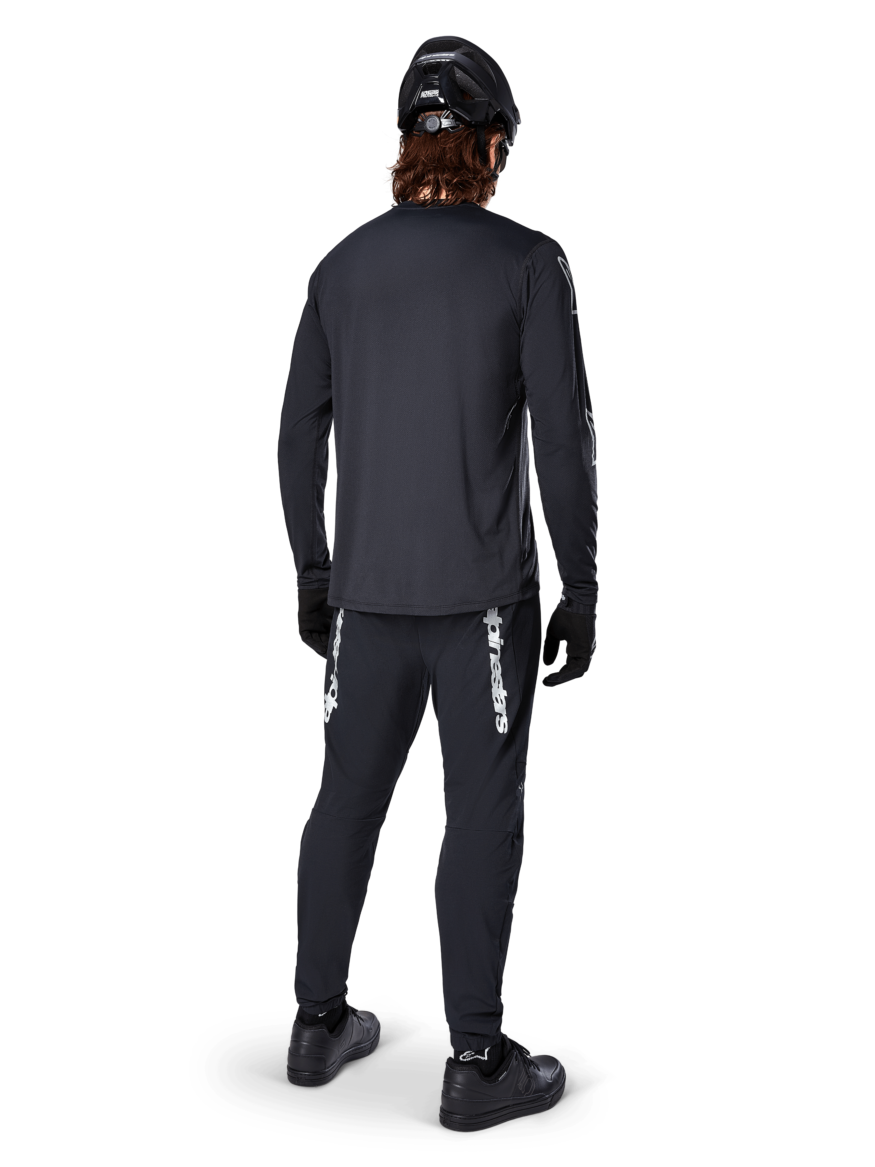 Maillot à manches longues Alpinestars A-Dura Switch, noir, vue arrière sur un cycliste, porté avec un pantalon noir arborant le marquage Alpinestars blanc, un casque noir et des gants, doté d'un pan arrière allongé pour une meilleure protection, vêtement de VTT haute performance