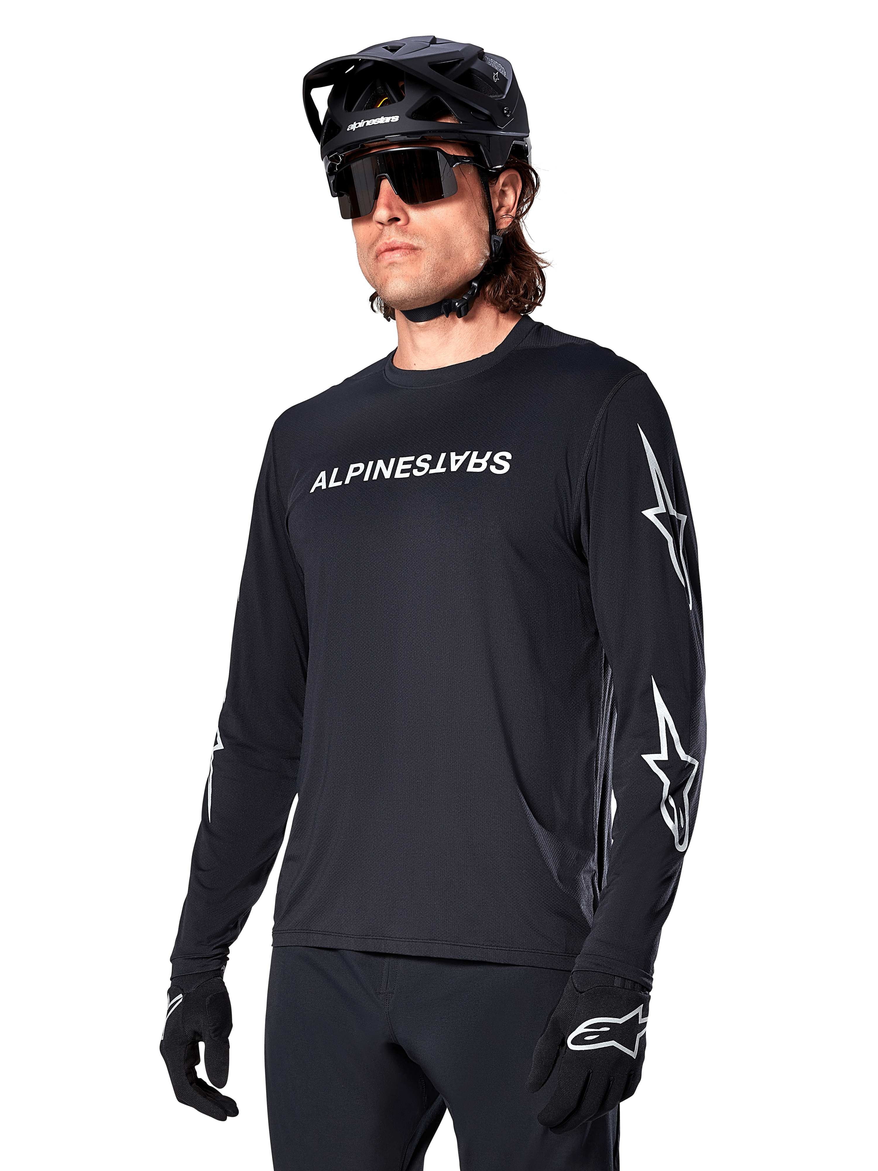 Cycliste masculin portant le maillot à manches longues Alpinestars A-Dura Switch, noir avec marquage blanc et logos étoiles sur les manches, avec casque de VTT noir et lunettes de soleil, équipement de cyclisme haute performance pour le tout-terrain