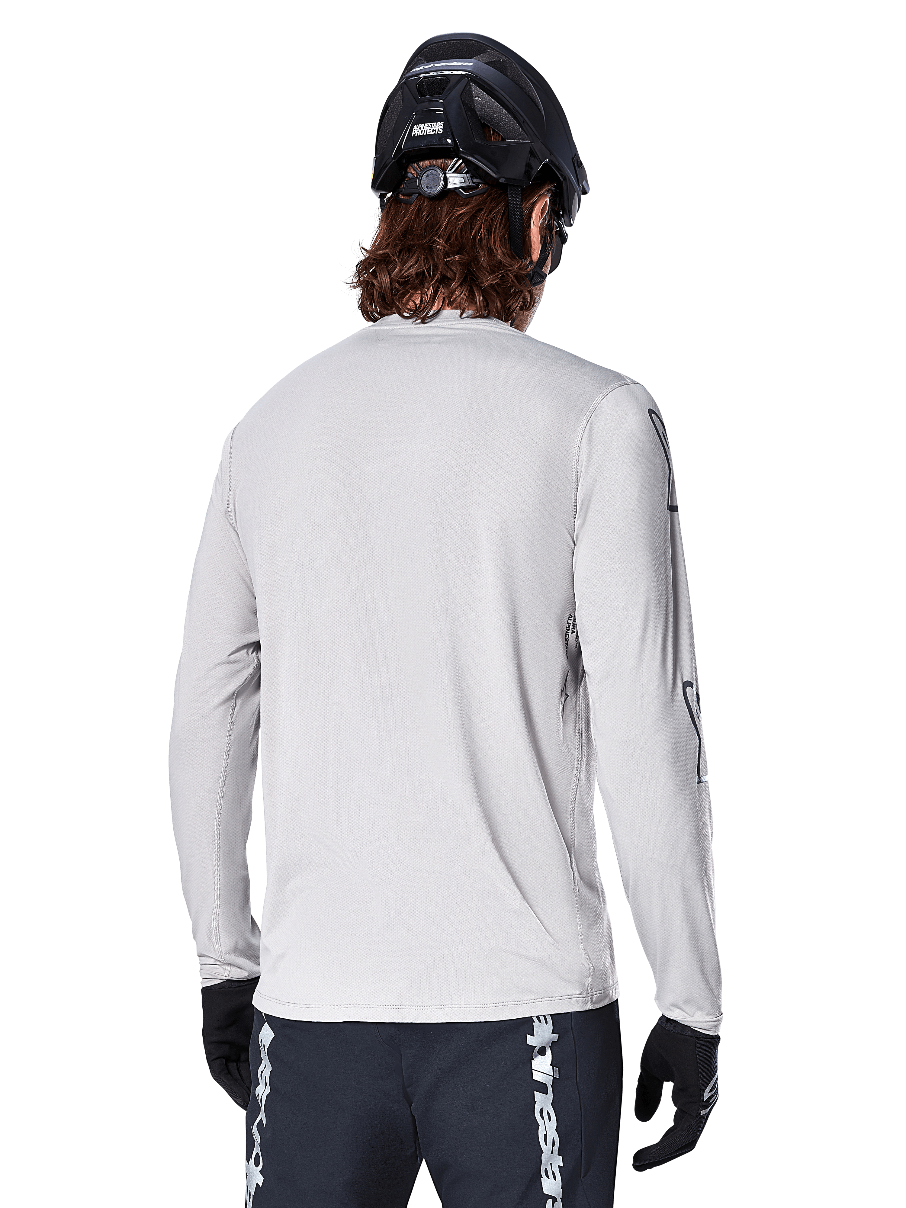 Maillot à manches longues Alpinestars A-Dura Switch, gris clair, vue arrière d'un vététiste portant un casque de VTT noir et des gants, avec une coupe arrière plus longue pour une protection accrue et un tissu jacquard texturé, équipement de cyclisme haute performance
