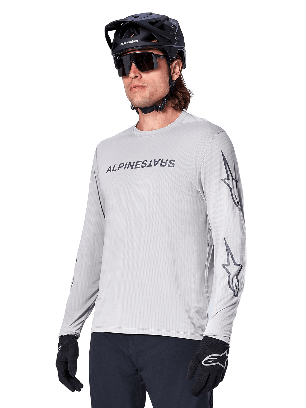 Maillot à manches longues Alpinestars A-Dura Switch, maillot de VTT, gris clair, inscription noire sur la poitrine et logos étoiles sur les manches, porté avec un casque de VTT noir, des lunettes de soleil sombres et des gants noirs, équipement de cyclisme tout-terrain athlétique