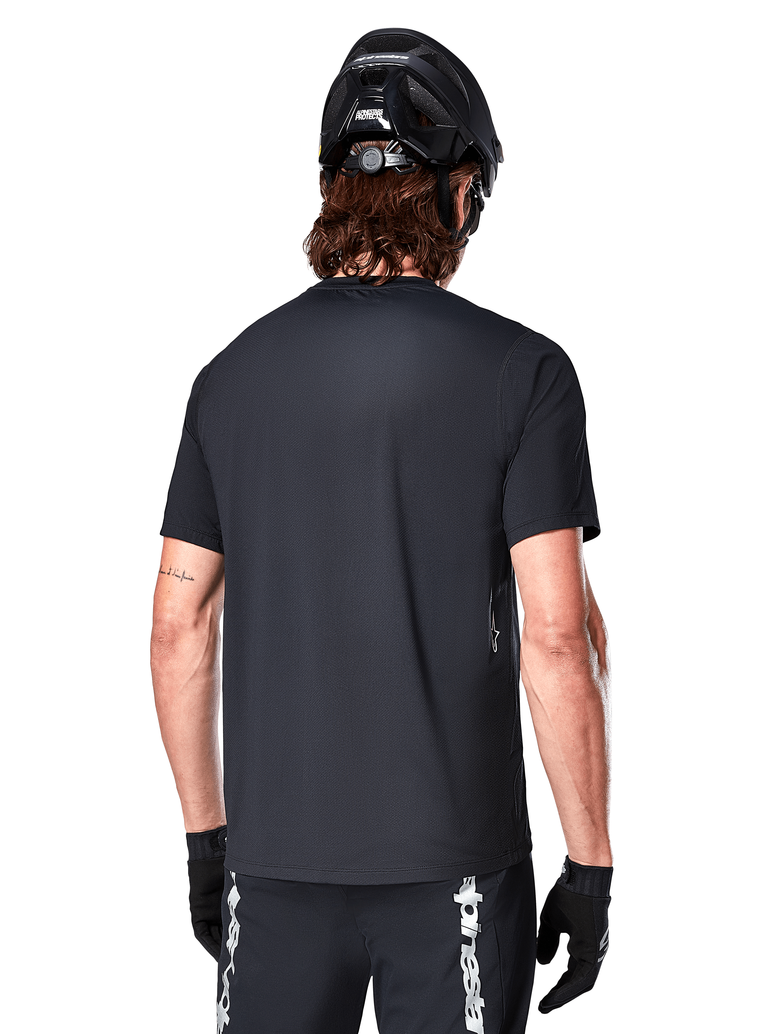 Alpinestars A-Dura Switch Jersey met korte mouwen, zwart, achteraanzicht op een model met een zwarte fietshelm en MTB-short, normale pasvorm en langere achterzijde voor mountainbiken