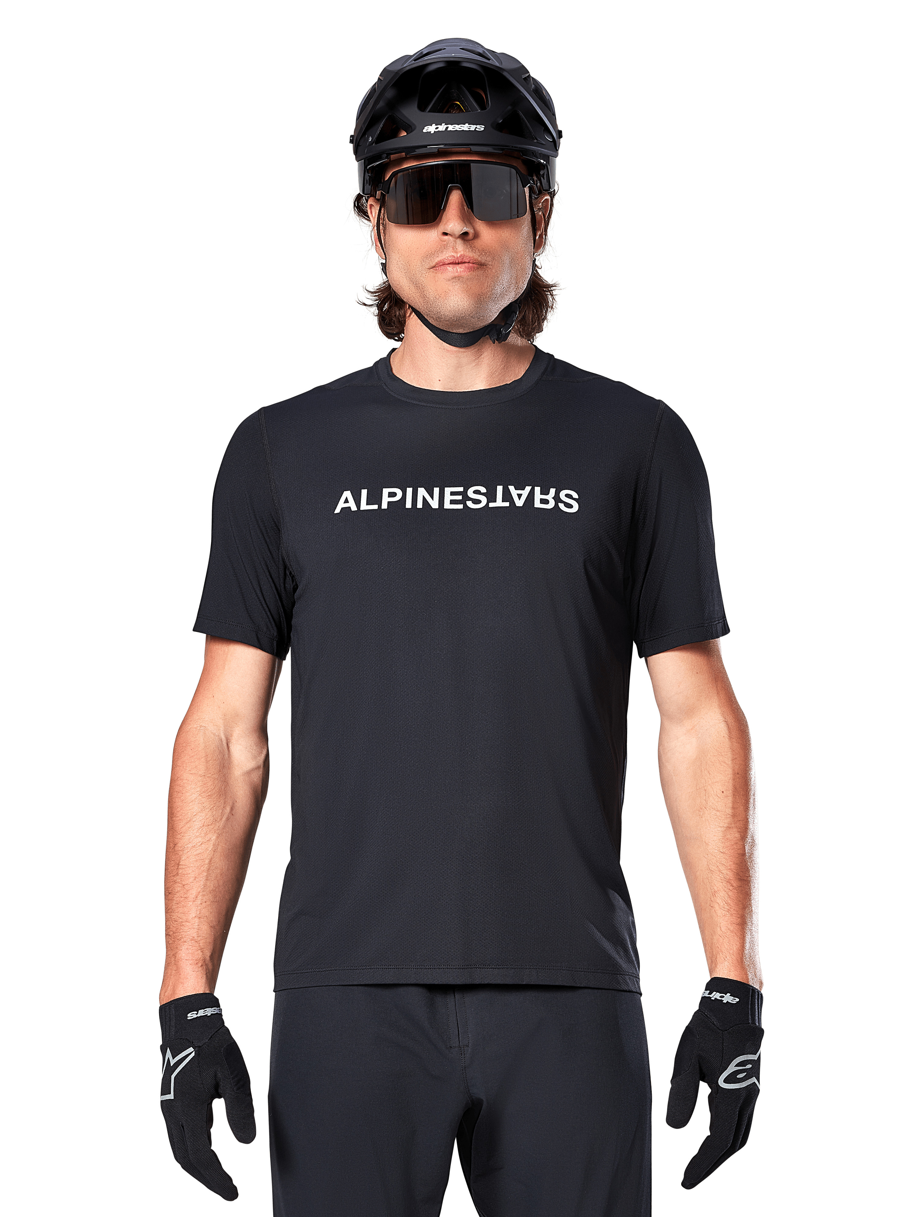 Mountainbiker die het Alpinestars A-Dura Switch Jersey met korte mouwen in het zwart draagt, met een wit woordmerklogo op de borst, gecombineerd met een zwarte helm, grote zonnebril en zwarte handschoenen, professionele fietskleding voor trailrijden.
