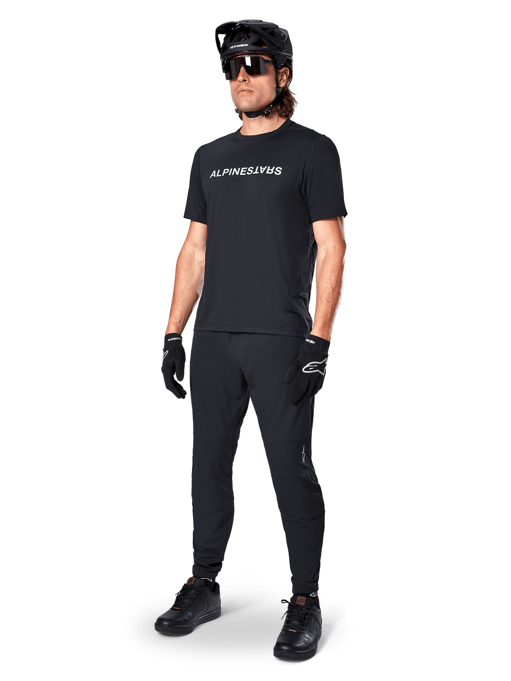 Alpinestars A-Dura Switch Jersey met korte mouwen, zwart, gedragen door model met bijpassende zwarte MTB-broek, helm en handschoenen, wit Alpinestars-woordmerk op de borst, hoogwaardige mountainbikekleding