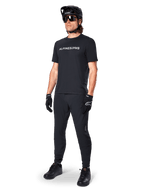 Alpinestars A-Dura Switch Jersey met korte mouwen, zwart, gedragen door model met bijpassende zwarte MTB-broek, helm en handschoenen, wit Alpinestars-woordmerk op de borst, hoogwaardige mountainbikekleding