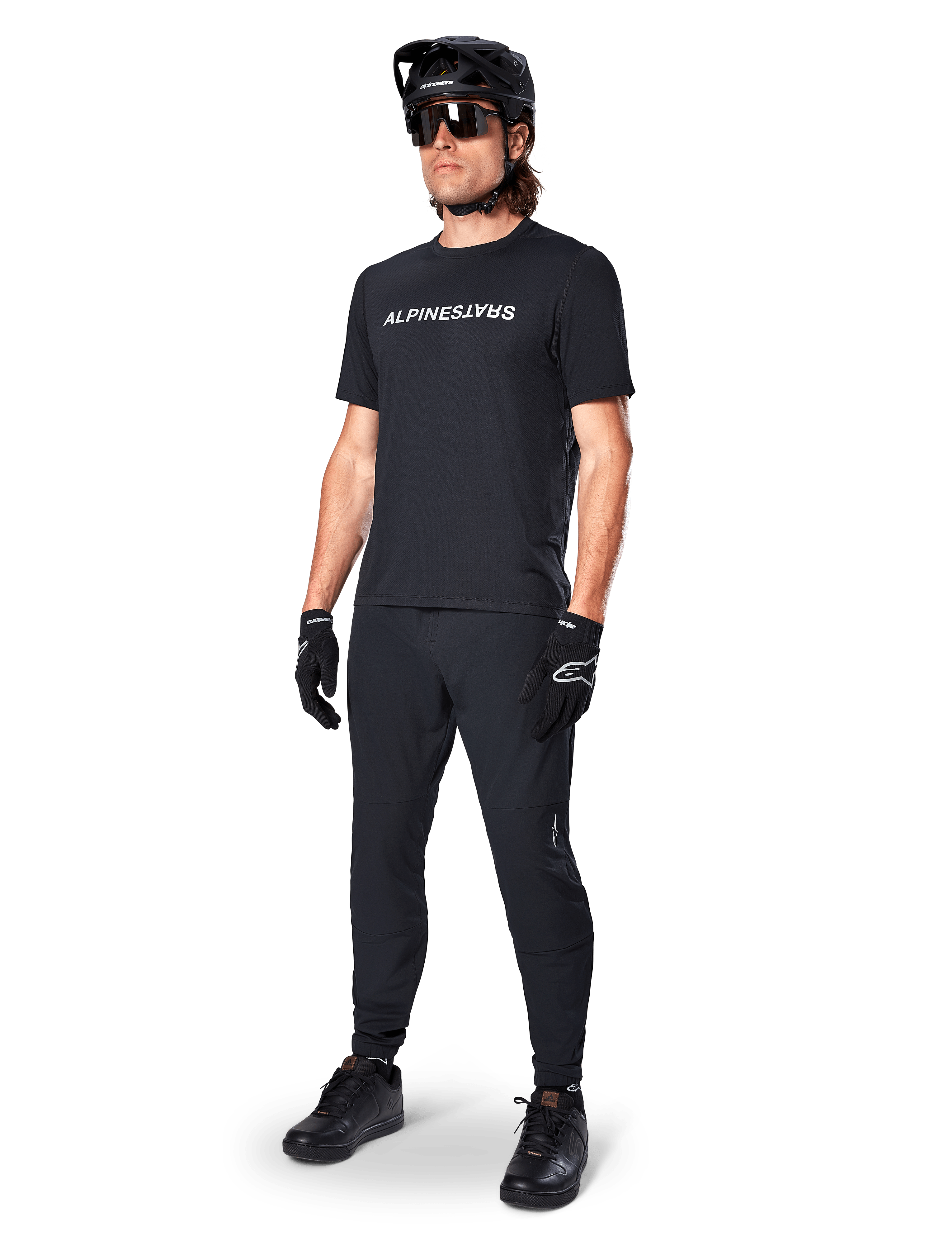Alpinestars A-Dura Switch Jersey met korte mouwen, zwart, gedragen door model met bijpassende zwarte MTB-broek, helm en handschoenen, wit Alpinestars-woordmerk op de borst, hoogwaardige mountainbikekleding