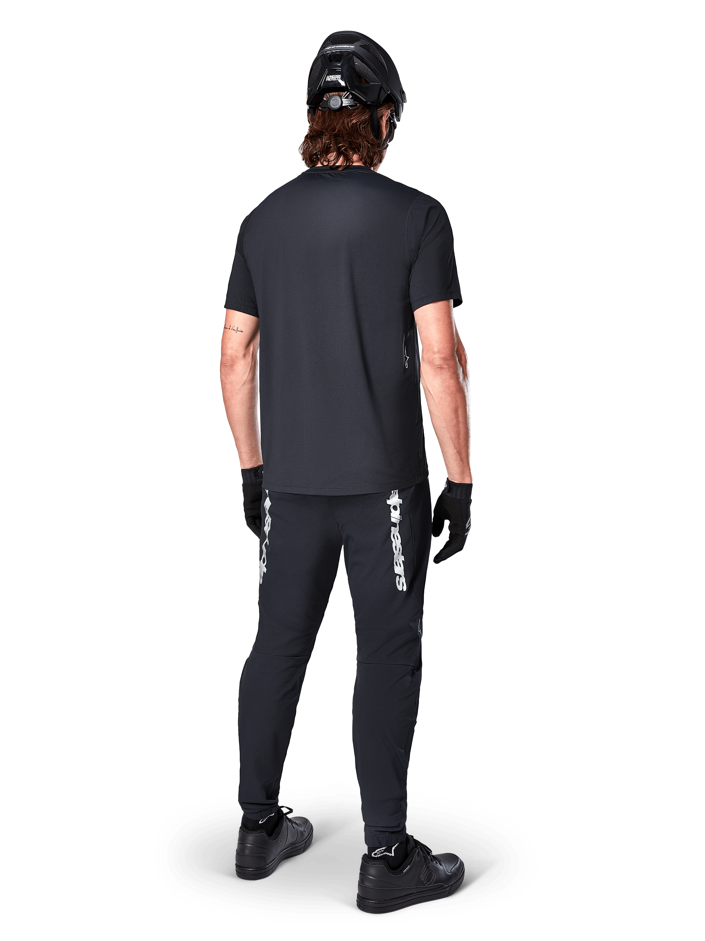 Alpinestars A-Dura Switch Jersey - Korte Mouwen, zwart, achteraanzicht van rijder in volledige mountainbike-uitrusting, inclusief bijpassende zwarte broek met wit woordmerk-logo, zwarte helm en handschoenen, technische fietskleding voor trailrijden