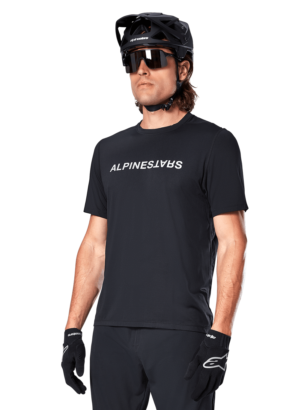 Alpinestars A-Dura Switch jersey met korte mouwen, zwart, wit woordmerklogo op de borst, gedragen door een fietser met zwarte MTB-helm en zonnebril, technische kleding voor trailrijden