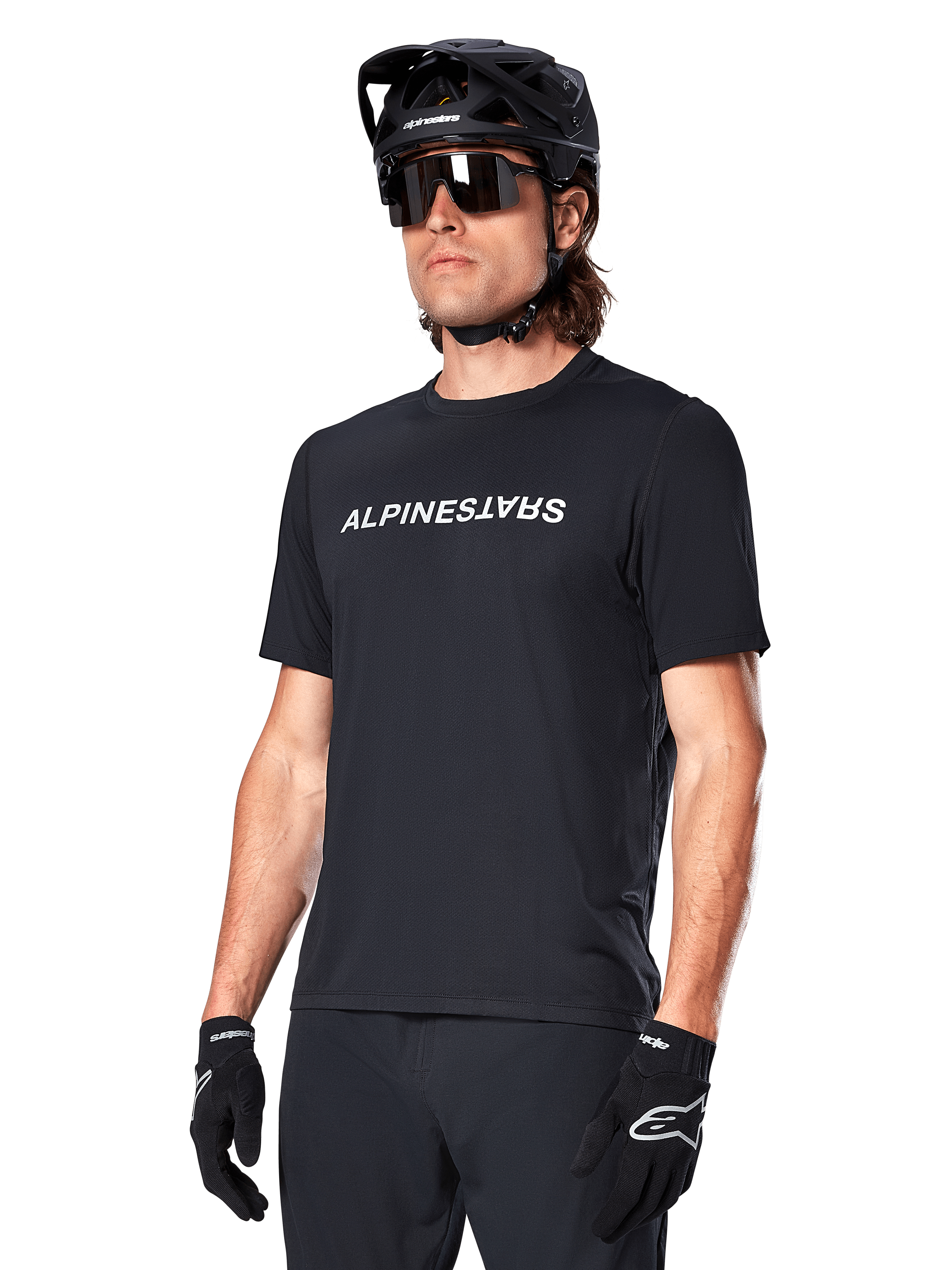 Alpinestars A-Dura Switch jersey met korte mouwen, zwart, wit woordmerklogo op de borst, gedragen door een fietser met zwarte MTB-helm en zonnebril, technische kleding voor trailrijden