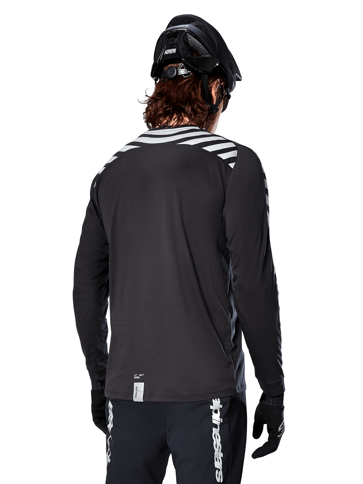 Maillot à manches longues Alpinestars A-Dura Dri Oscar, Noir réfléchissant, vue arrière montrant des rayures diagonales réfléchissantes sur les épaules et un pan arrière plus long, porté avec un casque et des gants de VTT noirs, équipement technique pour le VTT