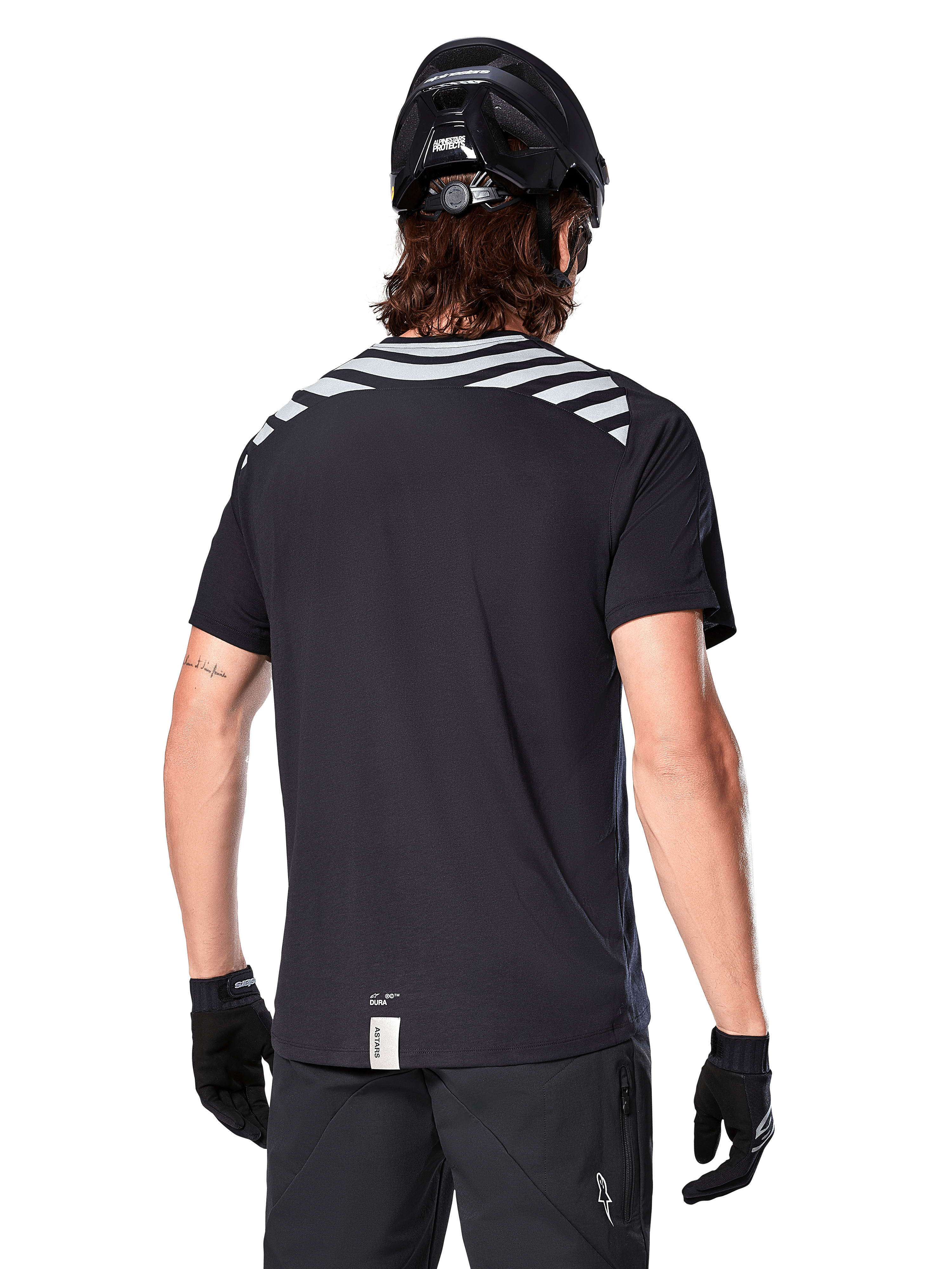 Alpinestars A-Dura Dri Oscar Trikot, Kurzarm-MTB-Trikot, Schwarz Reflektierend, Rückansicht am Model mit Fahrradhelm und Handschuhen, mit reflektierenden grauen Schulterstreifen und verlängertem Rückenteil, feuchtigkeitsableitendes Funktionsgewebe für Mountainbiking