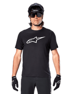 Alpinestars A-Dura Dri Oscar Kurzarmtrikot, Schwarz Reflektierend, getragen mit schwarzem MTB-Helm, Sonnenbrille und Handschuhen, mit markantem weißem Logo auf der Brust, Performance-Ausrüstung für Mountainbiking