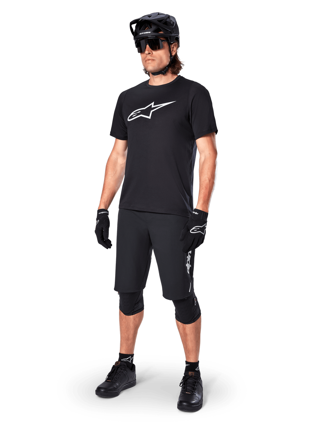Mountainbike-Fahrer im Alpinestars A-Dura Dri Oscar Kurzarmtrikot in Schwarz Reflektierend, mit einem großen weißen Logo auf der Brust, kombiniert mit passenden schwarzen MTB-Shorts, Handschuhen und Helm, technische Radsportbekleidung für Offroad-Performance