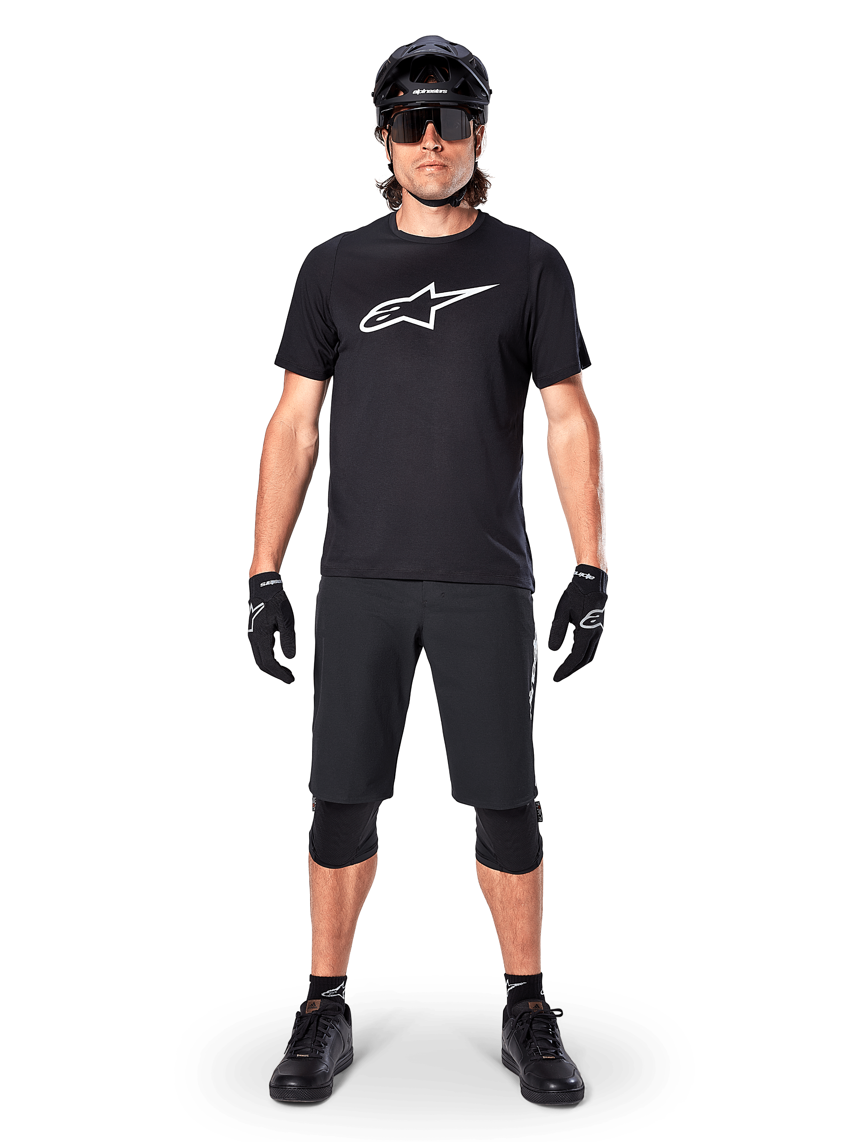 Alpinestars A-Dura Dri Oscar Kurzarmtrikot, Schwarz reflektierend, getragen mit passenden schwarzen MTB-Shorts, Handschuhen, Knieschützern und Helm, mit großem weißem Alpinestars-Logo auf der Brust, komplettes Mountainbike-Outfit