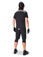 Alpinestars A-Dura Dri Oscar Kurzarmtrikot, Black Reflective, Rückansicht eines Fahrers mit schwarzen Mountainbike-Shorts, Helm und Knieschonern, reflektierende Schultergrafiken und verlängerte Rückenpartie für MTB-Fahrten.