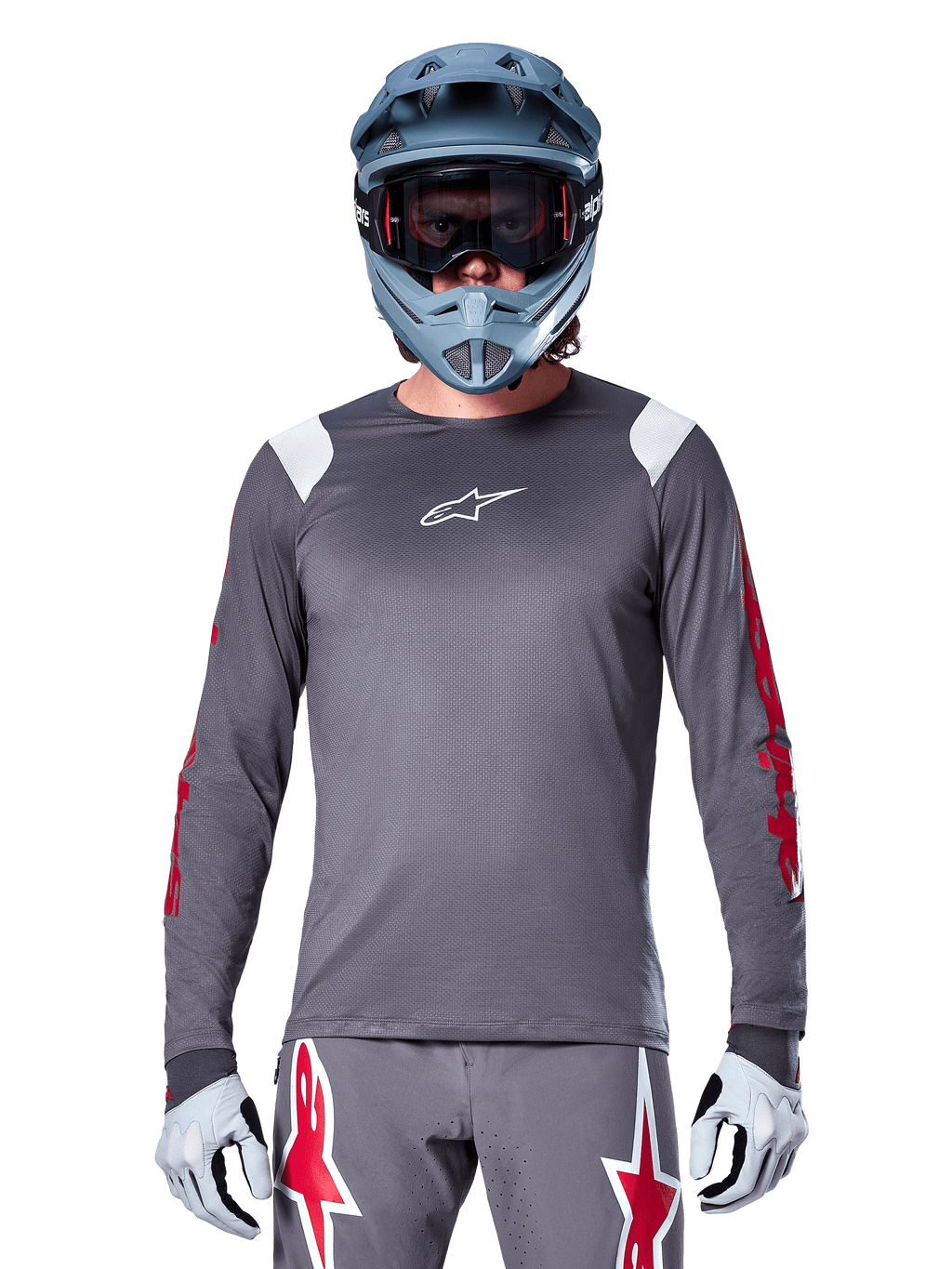 MTB-fietser in Alpinestars A-Supra Astar Jersey met lange mouwen, donkergrijs met rode graphics op de mouwen en witte schouderaccenten, bijpassende grijze broek met rode ster-logo's, blauwe full-face helm en goggle, gecoördineerde off-road wieleruitrusting