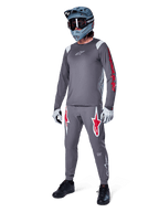 Alpinestars A-Supra Astar Jersey met lange mouwen, donkergrijs met rode branding op de mouwen en wit logo op de borst, gedragen door een rijder met bijpassende grijze broek, blauwgrijze full-face helm en handschoenen, complete mountainbike-uitrusting voor gravity riding.